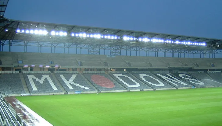 Chụp từ khán đài bên trong sân Stadium MK, cho thấy hàng ghế màu trắng và đỏ tạo thành chữ MK Dons