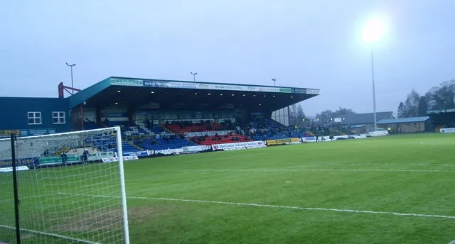 Khán đài East Stand tại sân Victoria Park, với hàng ghế nhựa xanh truyền thống và khung cảnh sân bóng.